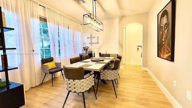 dining area featuring light wood-style flooring, visible vents, arched walkways, and baseboards