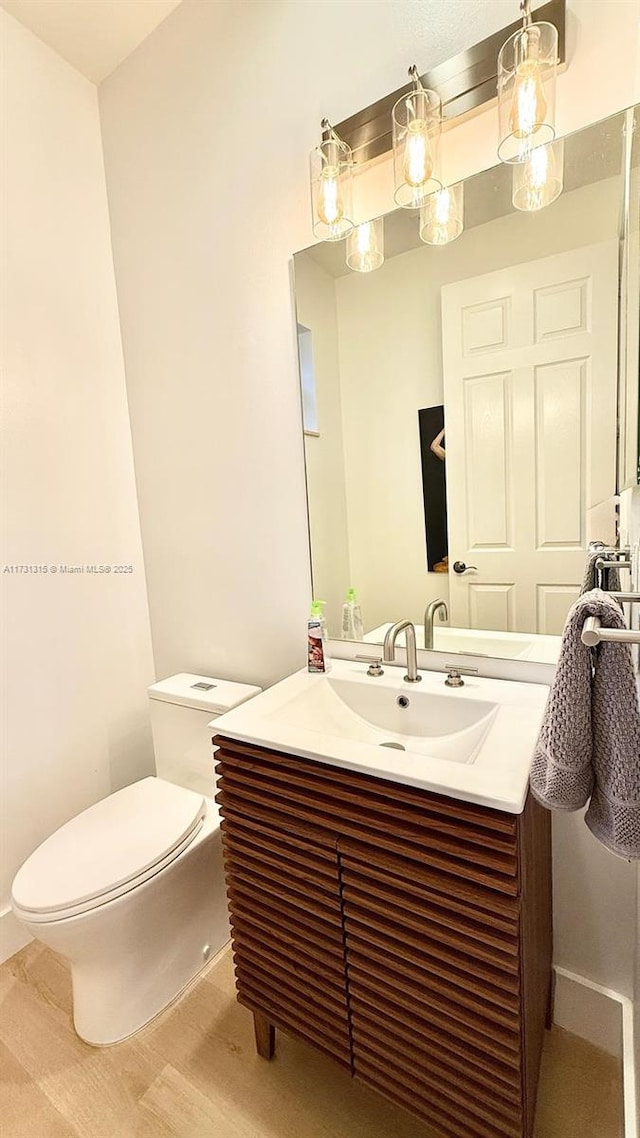 half bathroom featuring vanity, toilet, and wood finished floors