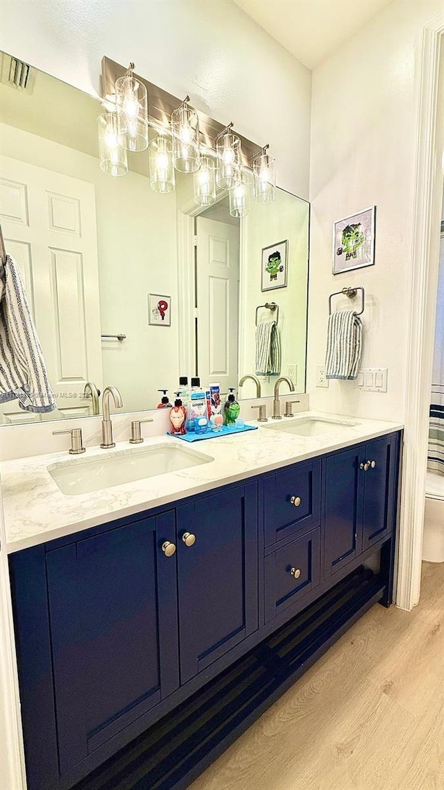 full bathroom featuring double vanity, visible vents, a sink, and wood finished floors