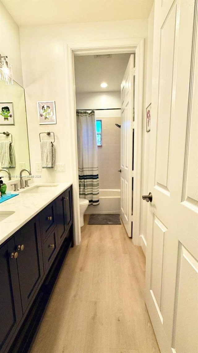 full bath with double vanity, toilet, shower / bath combo with shower curtain, a sink, and wood finished floors