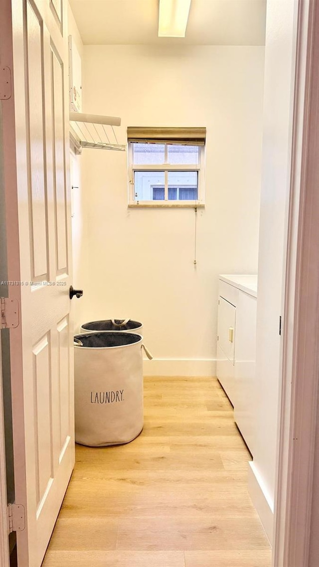 washroom featuring laundry area, baseboards, light wood finished floors, and washing machine and clothes dryer