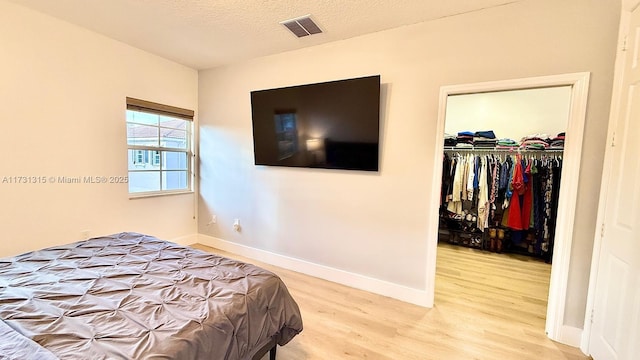 bedroom featuring visible vents, a spacious closet, a textured ceiling, light wood-type flooring, and baseboards