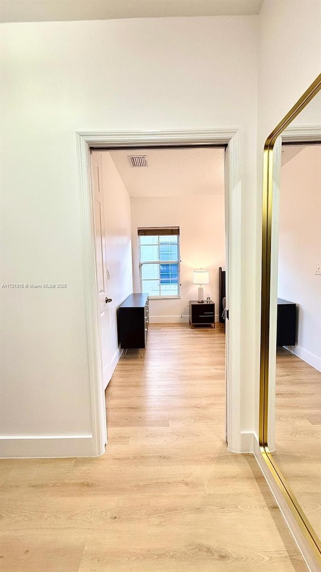 hall featuring visible vents, light wood-style flooring, and baseboards