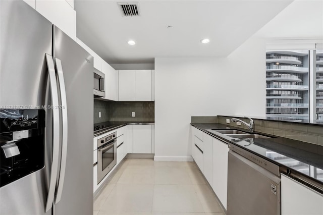 kitchen with sink, light tile patterned floors, appliances with stainless steel finishes, white cabinets, and decorative backsplash