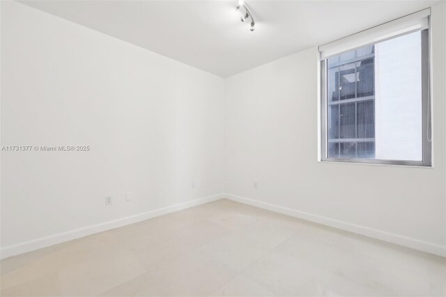 unfurnished room featuring rail lighting and baseboards