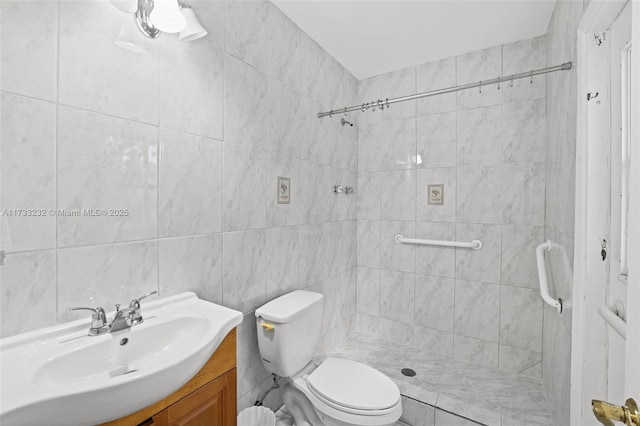 bathroom with tiled shower, vanity, toilet, and tile walls