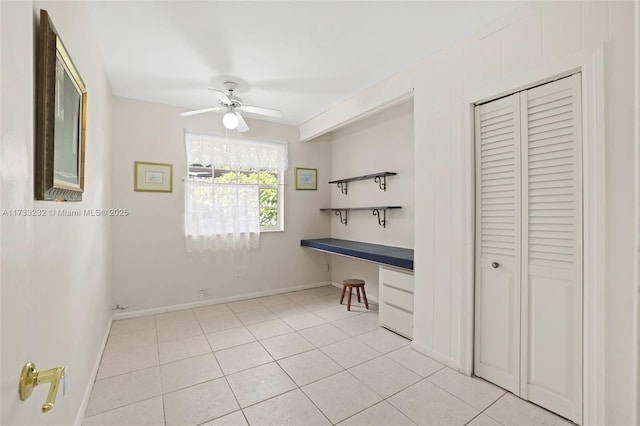 interior space featuring light tile patterned flooring, ceiling fan, built in desk, and a closet