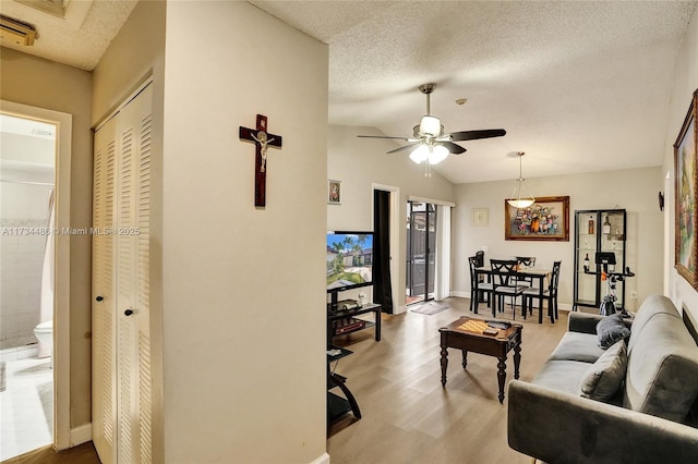 living room with ceiling fan, light hardwood / wood-style flooring, a textured ceiling, and vaulted ceiling