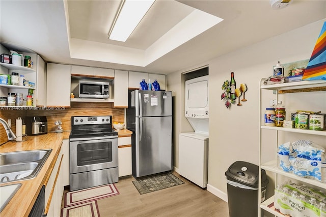 kitchen featuring stacked washer / drying machine, sink, butcher block countertops, white cabinetry, and appliances with stainless steel finishes