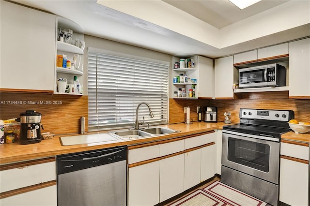 kitchen with appliances with stainless steel finishes, butcher block countertops, tasteful backsplash, sink, and white cabinets