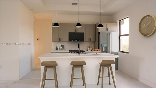 kitchen featuring a kitchen bar, high end fridge, gray cabinetry, a tray ceiling, and an island with sink