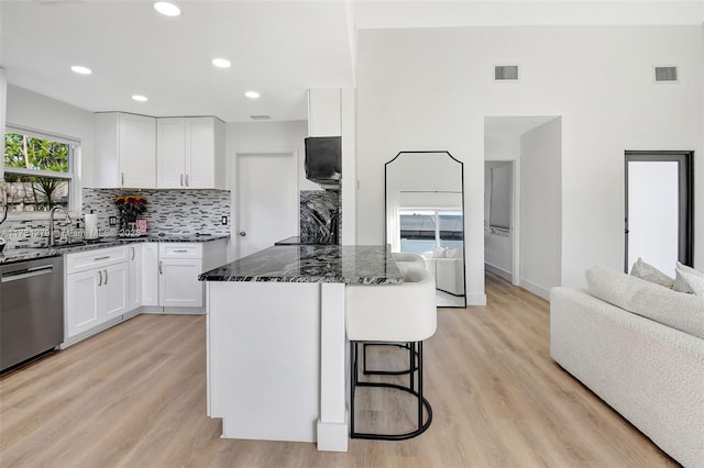 kitchen featuring white cabinetry, stainless steel dishwasher, a center island, and dark stone countertops