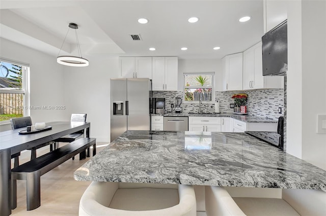 kitchen featuring dark stone countertops, appliances with stainless steel finishes, pendant lighting, and white cabinets