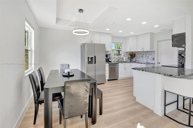 kitchen with appliances with stainless steel finishes, decorative light fixtures, white cabinetry, dark stone countertops, and light wood-type flooring