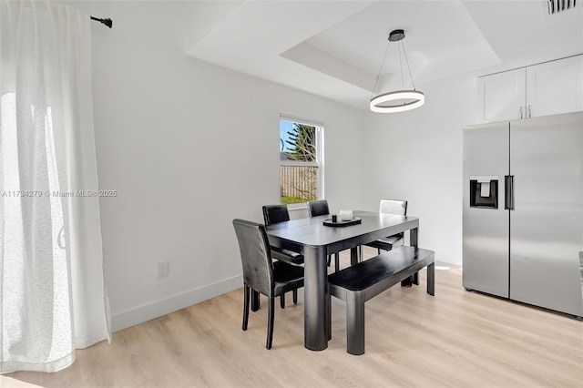 dining area with a tray ceiling and light hardwood / wood-style flooring