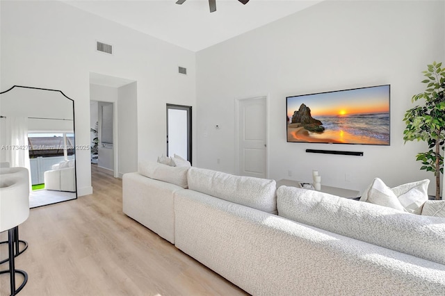 living room with ceiling fan, light hardwood / wood-style floors, and a towering ceiling