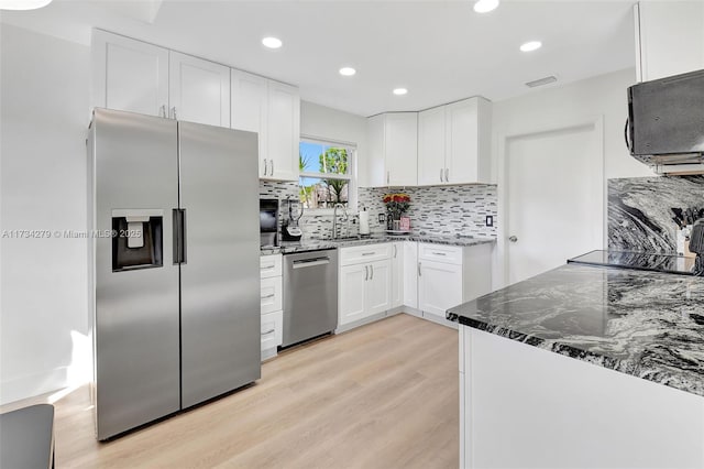 kitchen featuring white cabinetry, sink, dark stone countertops, stainless steel appliances, and light hardwood / wood-style flooring