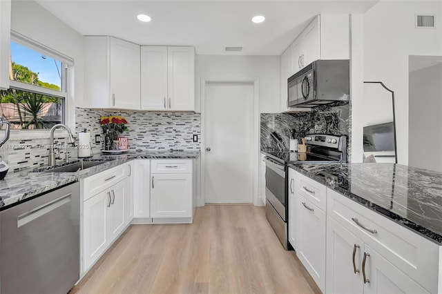 kitchen with appliances with stainless steel finishes, sink, dark stone countertops, and white cabinets