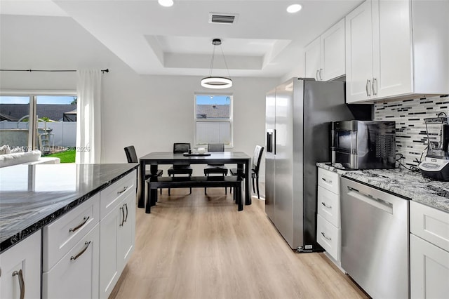 kitchen with white cabinetry, hanging light fixtures, dark stone countertops, stainless steel appliances, and a raised ceiling