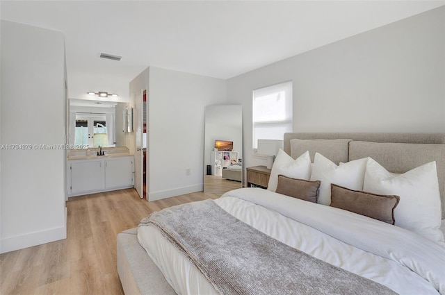 bedroom featuring ensuite bathroom, sink, light hardwood / wood-style floors, and multiple windows