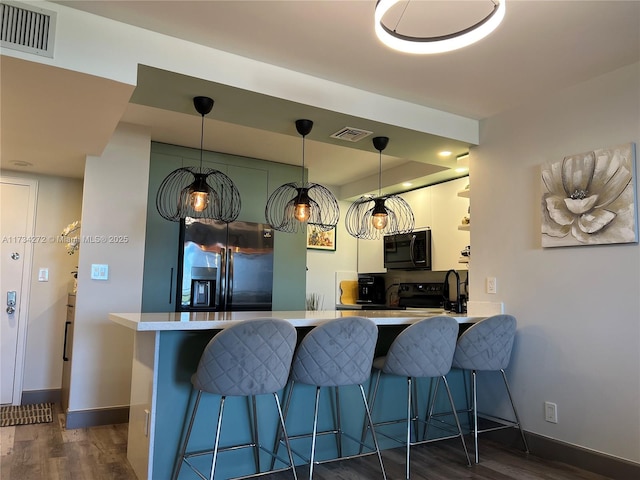 kitchen featuring kitchen peninsula, decorative light fixtures, a breakfast bar area, stainless steel fridge with ice dispenser, and dark wood-type flooring