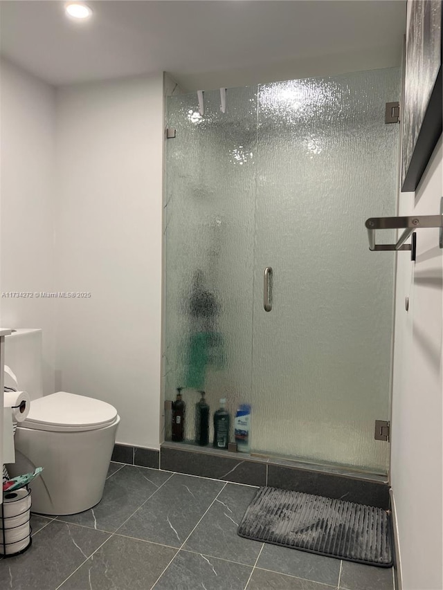 bathroom featuring a shower with shower door and toilet