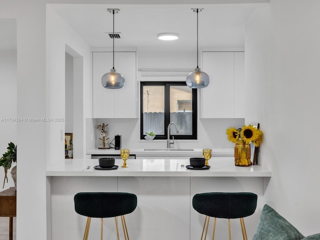 kitchen featuring white cabinetry, sink, decorative light fixtures, and a kitchen breakfast bar