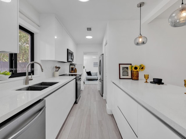 kitchen with appliances with stainless steel finishes, sink, pendant lighting, and white cabinets