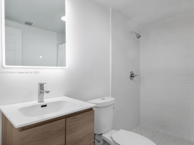 bathroom featuring vanity, a tile shower, and toilet