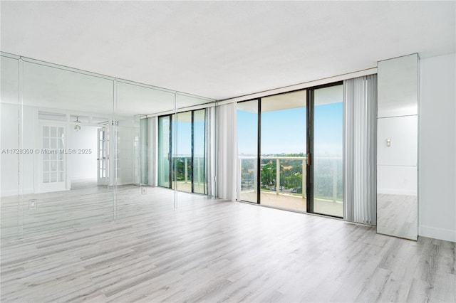 spare room with french doors, a healthy amount of sunlight, a wall of windows, and light hardwood / wood-style flooring