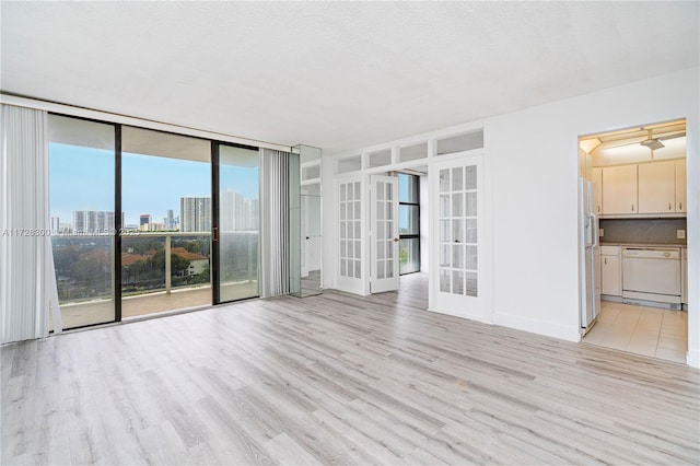 empty room with floor to ceiling windows, a textured ceiling, light wood-type flooring, and french doors