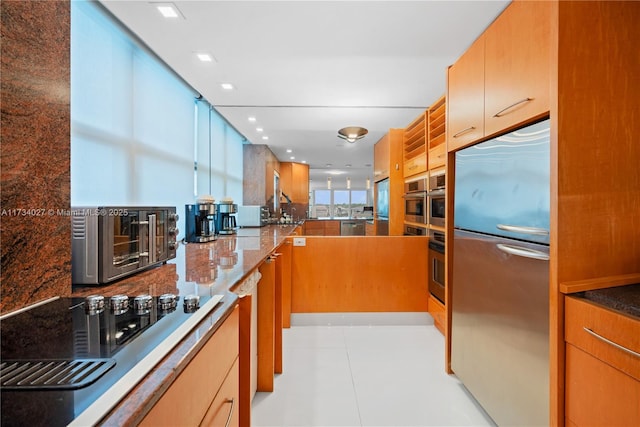 kitchen featuring stainless steel appliances, light tile patterned floors, and dark stone countertops