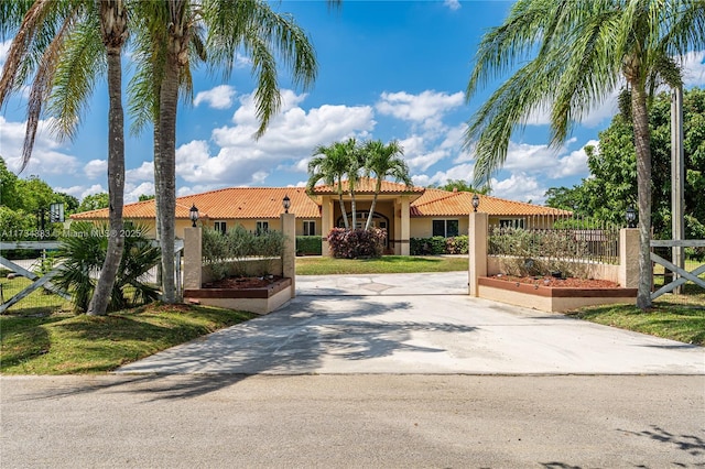 mediterranean / spanish home with concrete driveway, stucco siding, a tile roof, fence, and a front yard