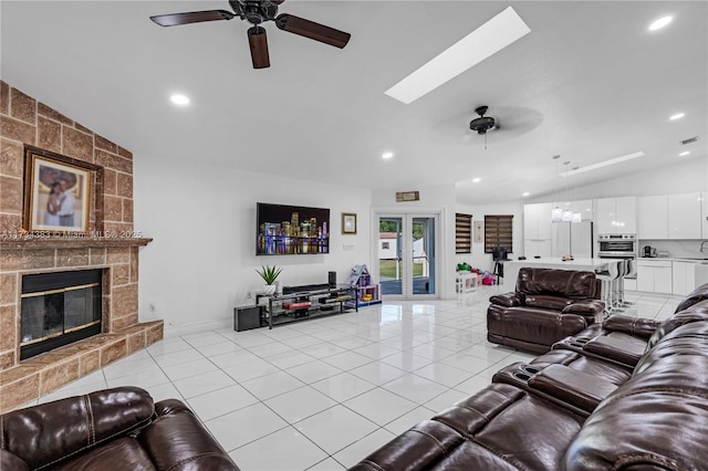 living area with light tile patterned floors, ceiling fan, a large fireplace, french doors, and lofted ceiling with skylight