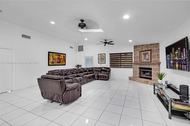 living area with light tile patterned floors, visible vents, a ceiling fan, vaulted ceiling, and a stone fireplace