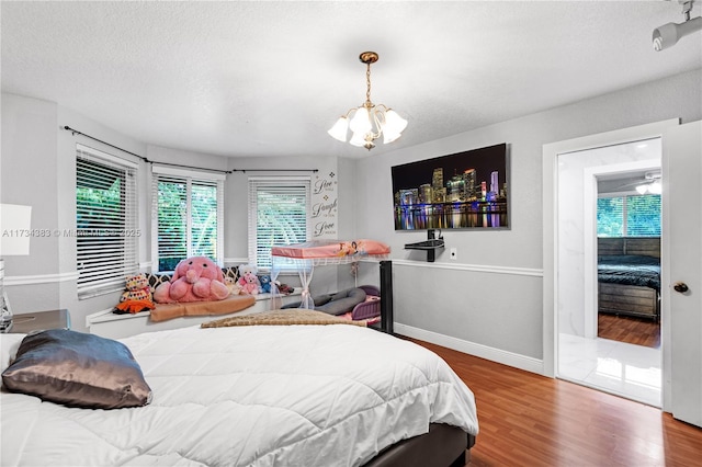 bedroom featuring a textured ceiling, baseboards, wood finished floors, and a notable chandelier