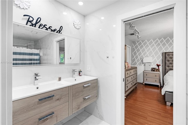 bathroom featuring double vanity, a sink, ensuite bath, and wood finished floors