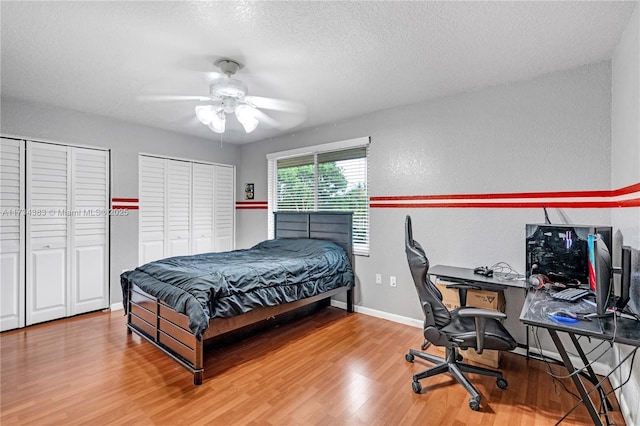 bedroom featuring multiple closets, a textured ceiling, baseboards, and wood finished floors