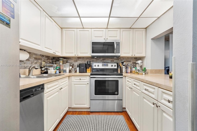 kitchen featuring sink, a paneled ceiling, white cabinets, stainless steel appliances, and backsplash