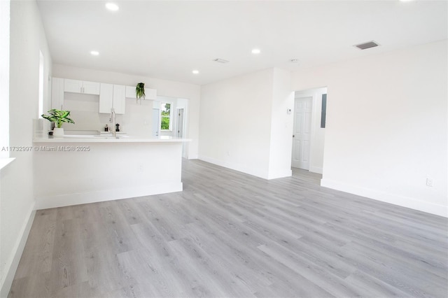 kitchen with white cabinetry, sink, light wood-type flooring, and kitchen peninsula