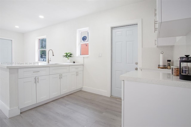 kitchen featuring sink, white cabinets, light wood-type flooring, and kitchen peninsula