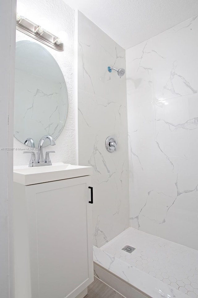 bathroom with hardwood / wood-style flooring, vanity, tiled shower, and a textured ceiling