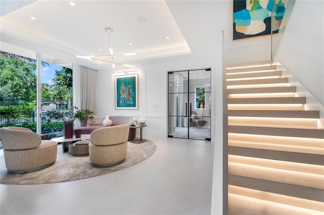 interior space with a tray ceiling, stairway, a notable chandelier, and finished concrete flooring