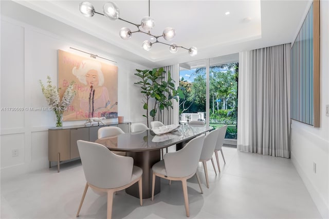 dining space with an inviting chandelier, a raised ceiling, a decorative wall, and concrete flooring