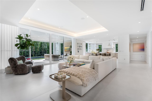 living room with a raised ceiling, recessed lighting, visible vents, and expansive windows