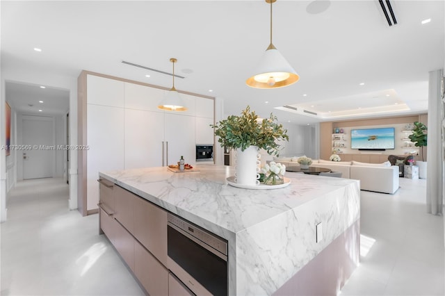 kitchen with white cabinetry, stainless steel microwave, modern cabinets, a raised ceiling, and a center island