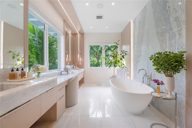 full bath with a wealth of natural light, a soaking tub, vanity, and visible vents