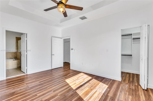 unfurnished bedroom with a closet, hardwood / wood-style flooring, a raised ceiling, and a spacious closet