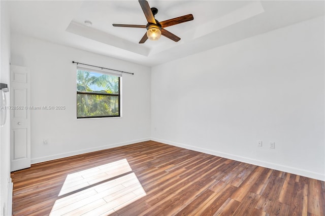 unfurnished room with hardwood / wood-style flooring, ceiling fan, and a tray ceiling