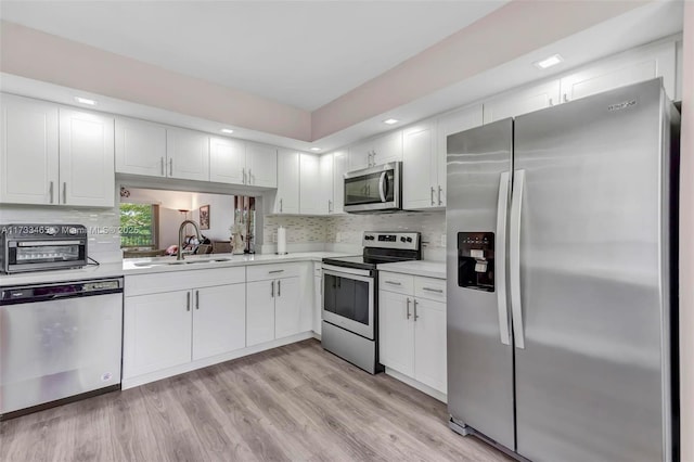 kitchen with sink, light wood-type flooring, appliances with stainless steel finishes, white cabinets, and backsplash